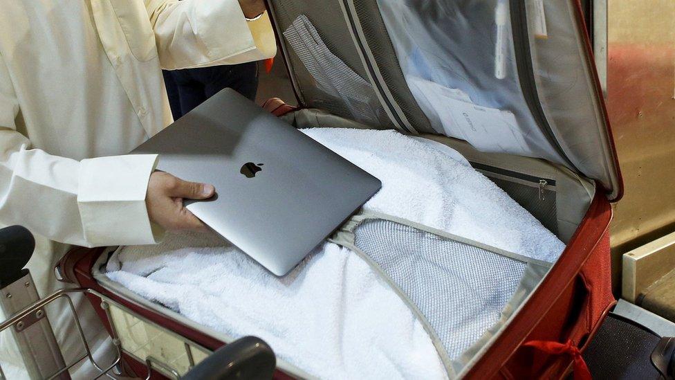 A man places a laptop in a suitcase at Kuwait International Airport, 23 March 2017