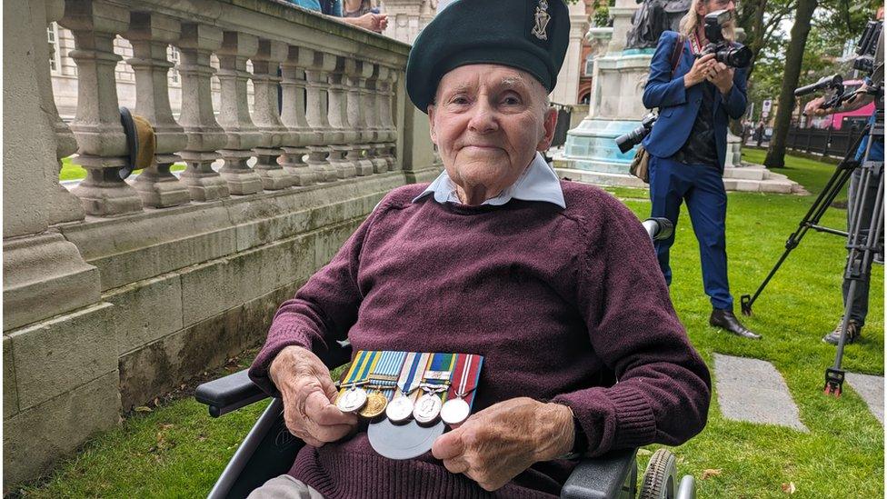 Lance Corporal Albert Morrow, wearing a green Royal Ulster Rifles cap, sits in his wheelchair holding his medals