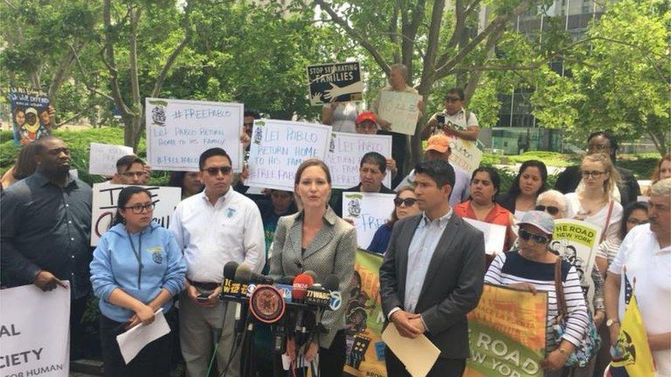 Lawyer speaks to press, protesters with signs behind her