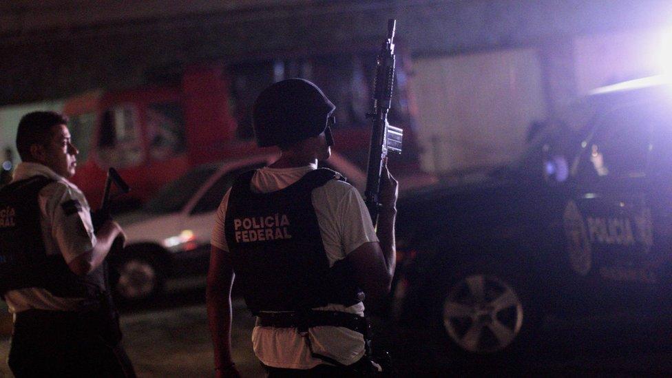 Man in helmet and bulletproof holds machine gun in air; it's night time; the black vest contrasts with his white short sleeved T shirt