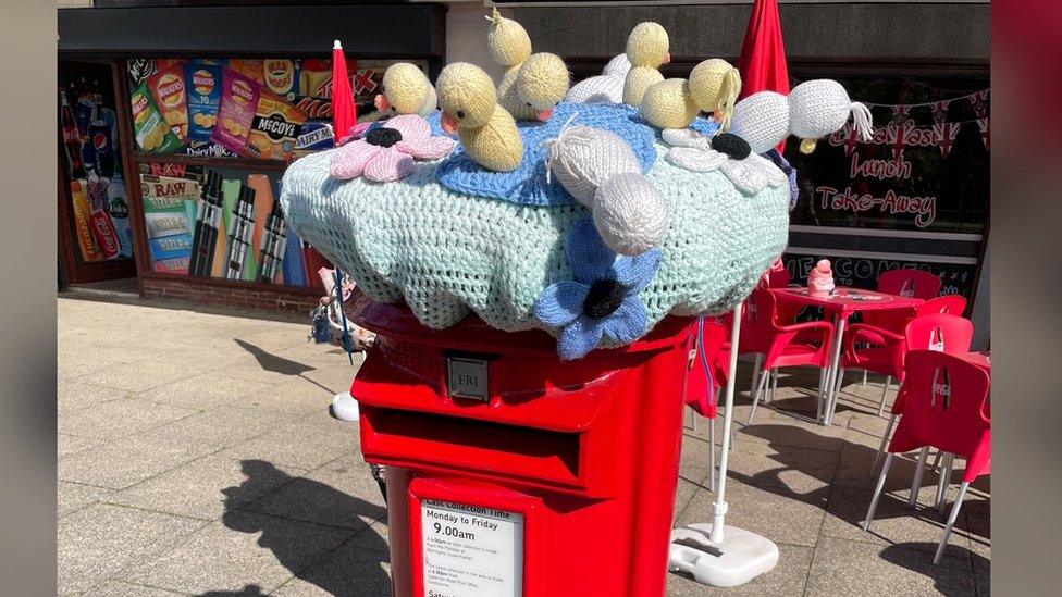 A knitted post box topper of chicks and flowers in Hampden Park