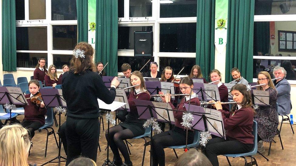 Student orchestra playing in school auditorium in front of a conductor