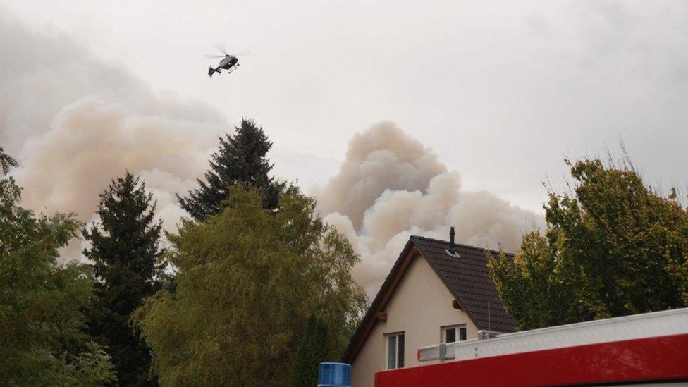 Smoke rises from a forest fire, as a police helicopter flies over a house in a nearby village