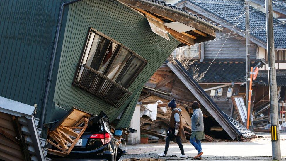 Residents walk past a damaged house, following an earthquake, in Nanao, Ishikawa prefecture, Japan 2 January 2024