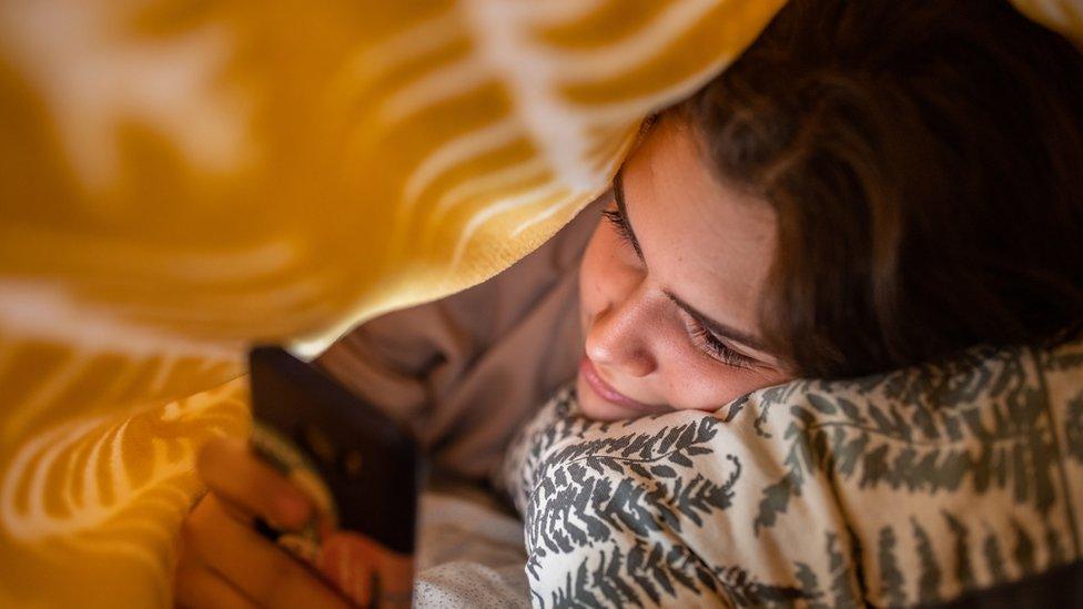 A girl using her mobile phone under the bed sheet