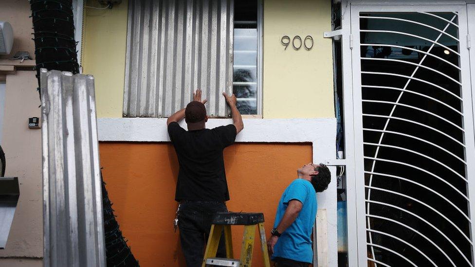 Workers place hurricane shutters over windows in Florida