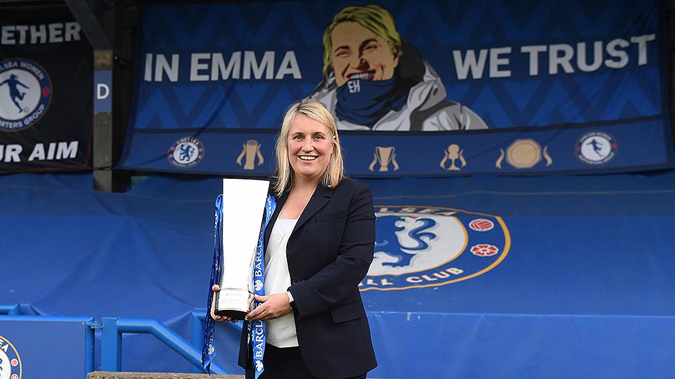 Emma Hayes lifting trophy with fan banner behind