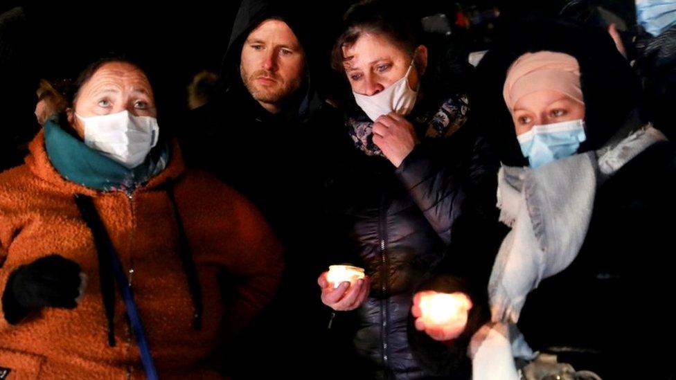 People gather near candles and flowers to pay tribute to the 27 migrants who died at the Richelieu Parc in Calais, France