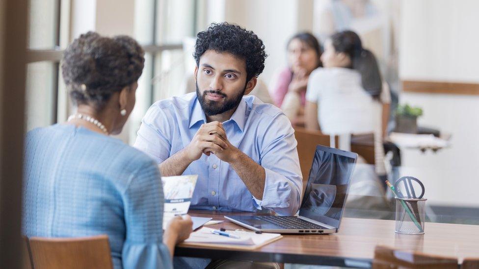 Mature female bank customer discusses opening a savings account with a bank employee