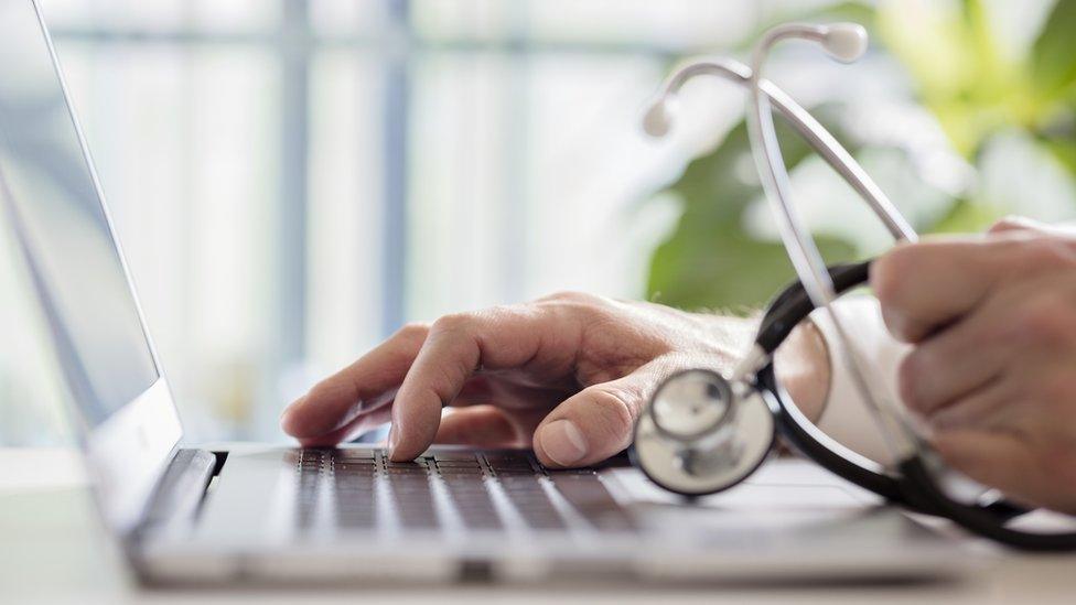 A GP using a laptop computer while holding a stethoscope