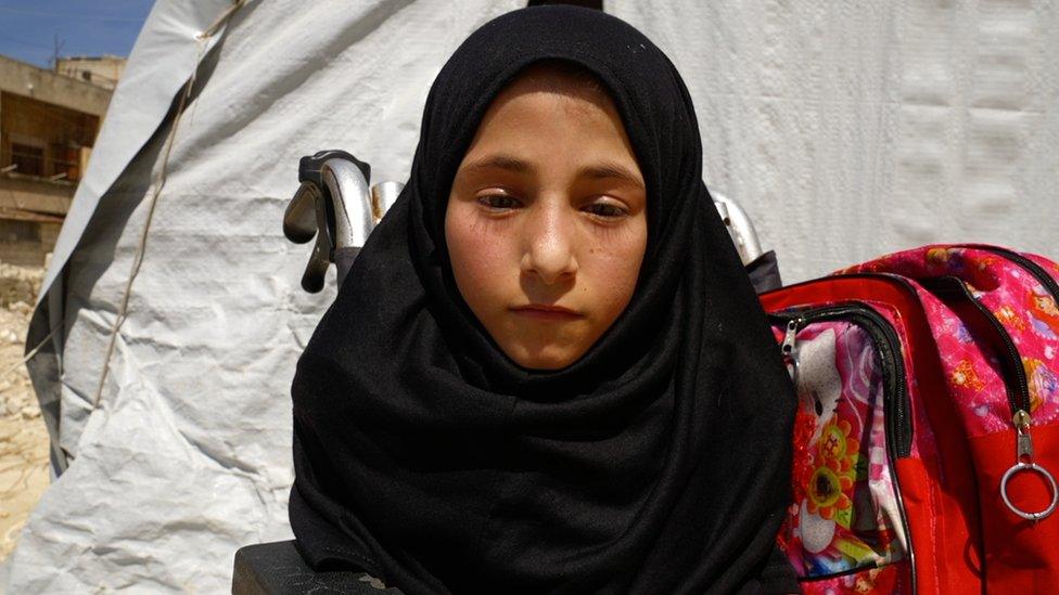 A girl in a wheelchair sits in front of a white tent