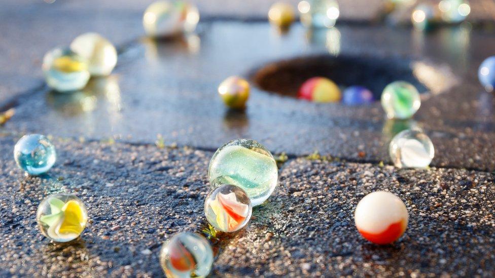 All kinds of colored glass marbles in the light of the setting sun on the pavement with a marble pot in the tile.