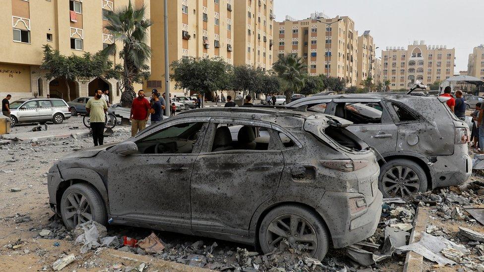 Palestinians look at damaged vehicles near the site of Israeli strikes on a house in Khan Younis in the southern Gaza Strip, 23 October, 2023