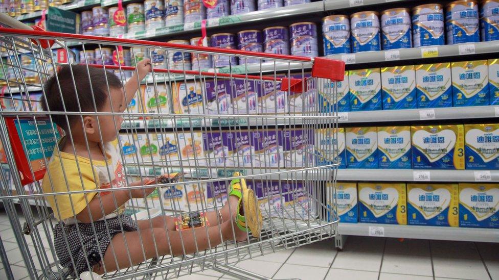 A baby stays in a shopping cart as his mother selects baby milk in a supermarket in Haikou, south China's Hainan province