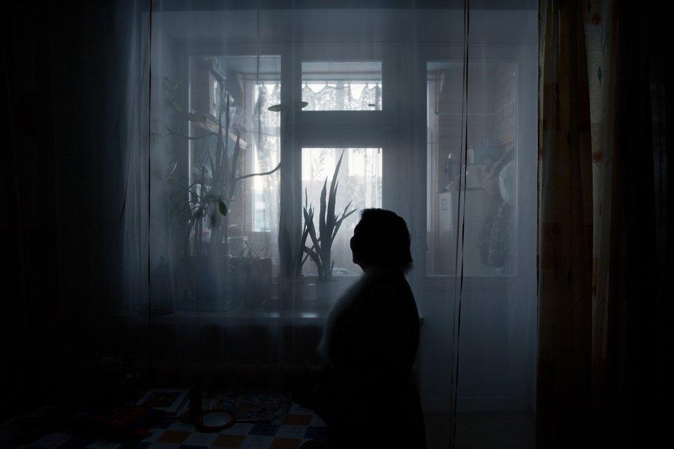 Liliya Yamkina (Born. 1944) looking through the window in her apartment. Yar-Sale village, Yamal Peninsula, Siberia, Russia.