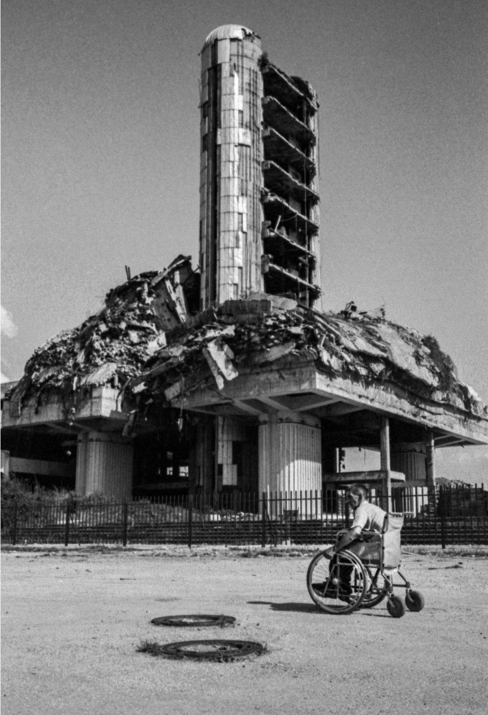 A view of a war torn building with a man in a wheelchair in front of it