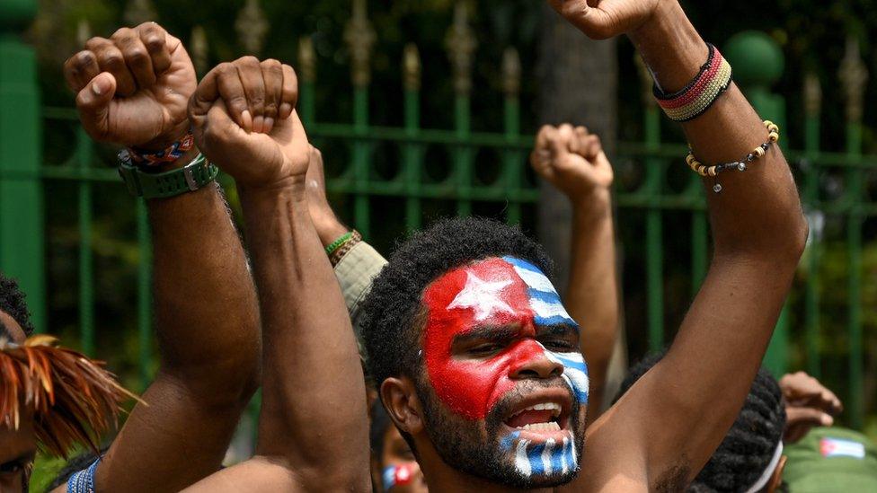 Protesters raising their fists with the Morning Star flag, a symbol of independence, painted on their face