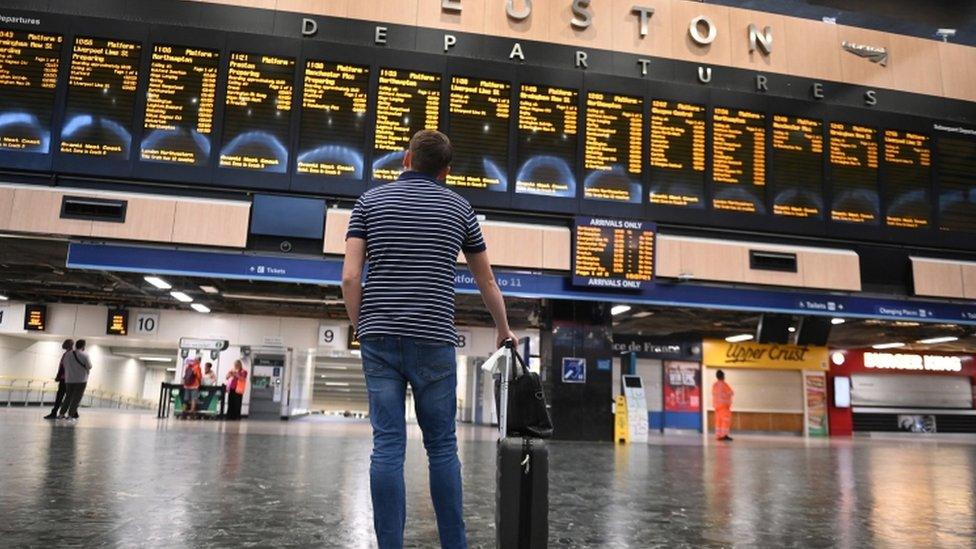 man stood looking at cancelled trains on board at Euston station