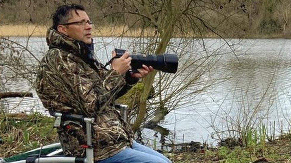 Jon Kelf sitting on his all terrain walker, looking out over a stretch of water while holding his camera