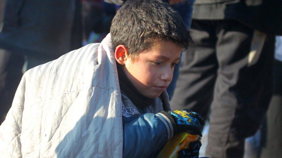 A boy sits huddled in a blanket