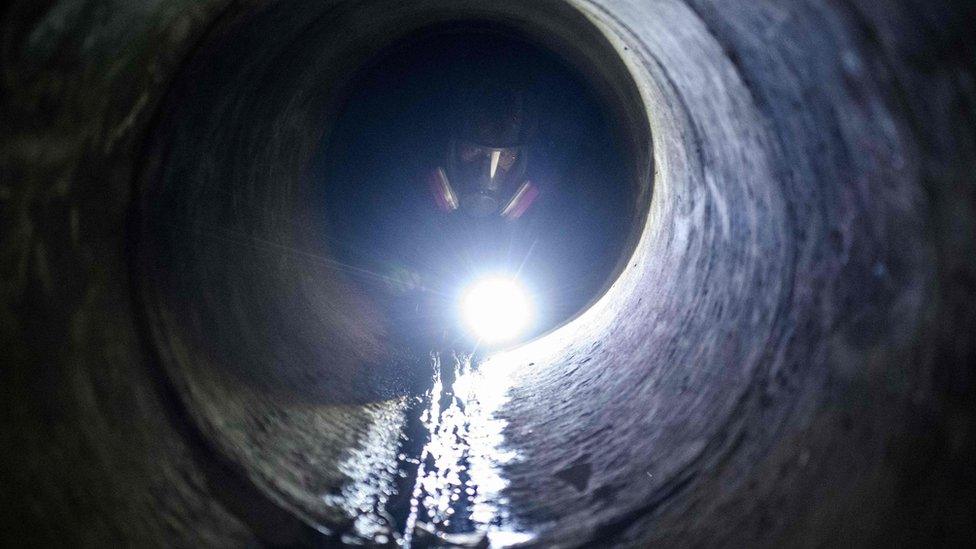 A protester uses a torch light while crawling within a sewer tunnel to see how wide it is