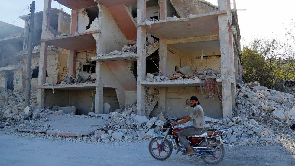 A Syrian man rides a motorbike past a building reportedly damaged by an air strike in Jisr al-Shughour (4 September 2018)