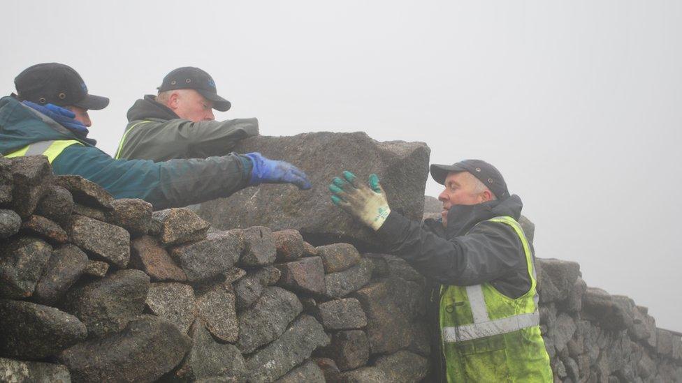 The men lift a capping stone on to the top of the wall close to the summit of Slieve Donard