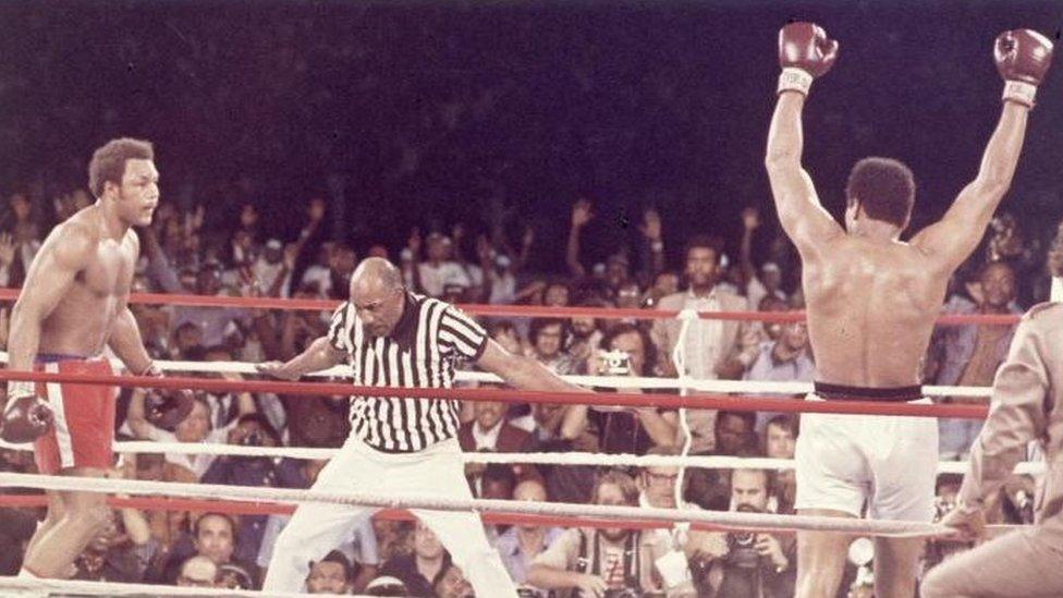 Muhammad Ali, arms raised in victory, walks to his corner as referee Zack Clayton counts out George Foreman after Ali knocked him down in the eighth round of their Rumble in the Jungle title bout in Kinshasa, Zaire (29 October 1974)