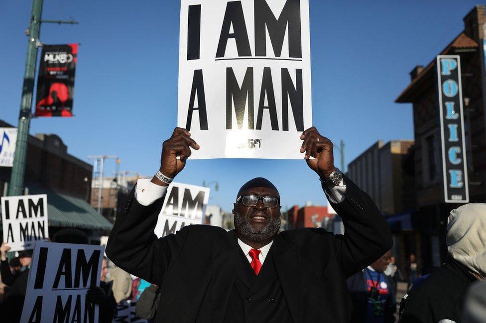 A man holds a sign declaring 'i am a man'