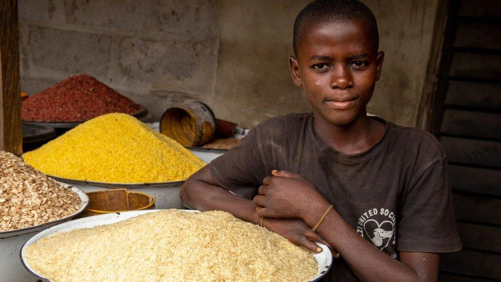 A young boy poses next to some rice in his shop at Ajara Market in Badagry, near Lagos, on September 6, 2019