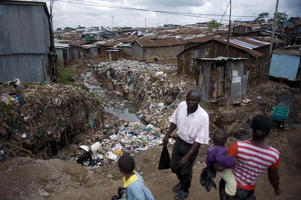 Residents of Kibera walk past an open sewer