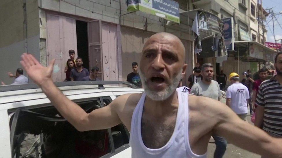 A man talks to media standing next to a car that was hit by rockets