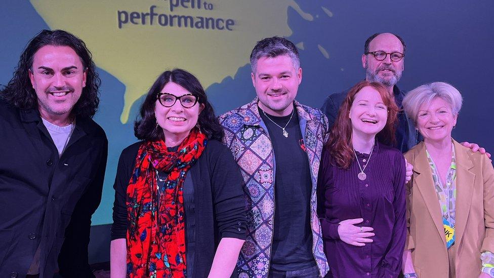 Six people stand on stage in front of a yellow splat logo for the Ink Festival