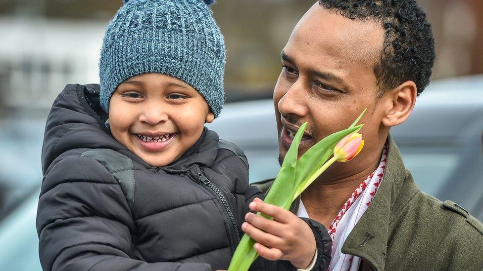 A father holds his son, who is clutching flowers