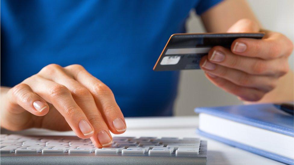 Person holding credit card while using computer