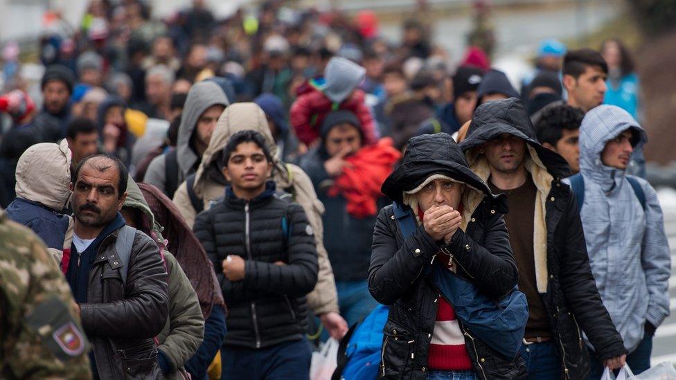 Refugees and migrants walk down a road to cross the Slovenian-Austrian border