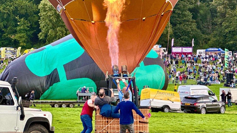 Hot air balloons filling on the ground, one orange, another green and black