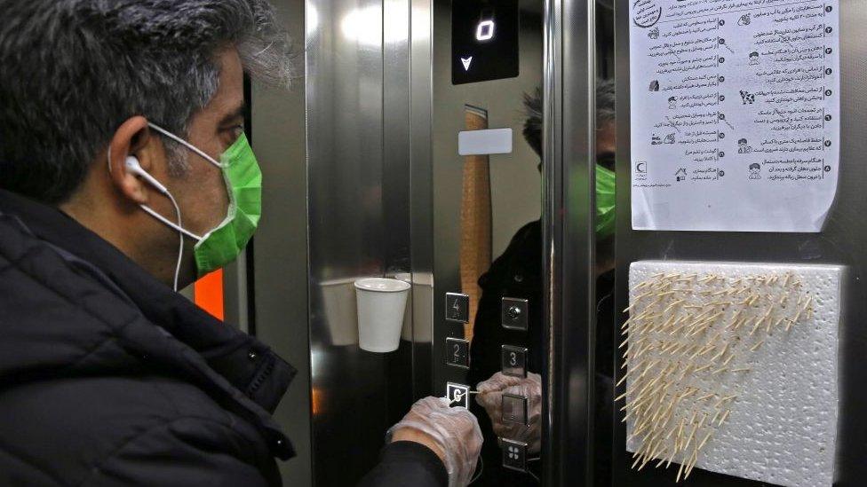 An Iranian man uses small sticks to push the elevator button at an office building in Tehran on March 4, 2020