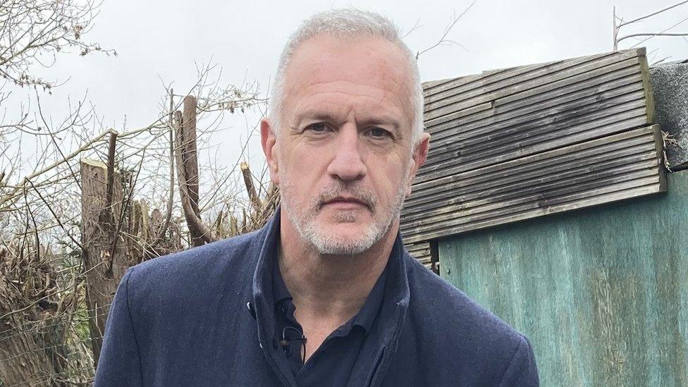 Ian Boulton standing outside in front of a broken fence