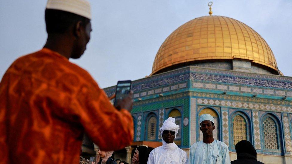 Two people posing while a third takes a picture of them in front of the golden dome of al-Aqsa mosque, Jerusalem.