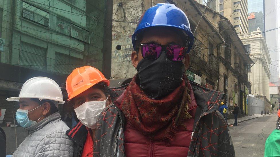 Protester Marcos poses for a photograph in a blue helmet and sunglasses