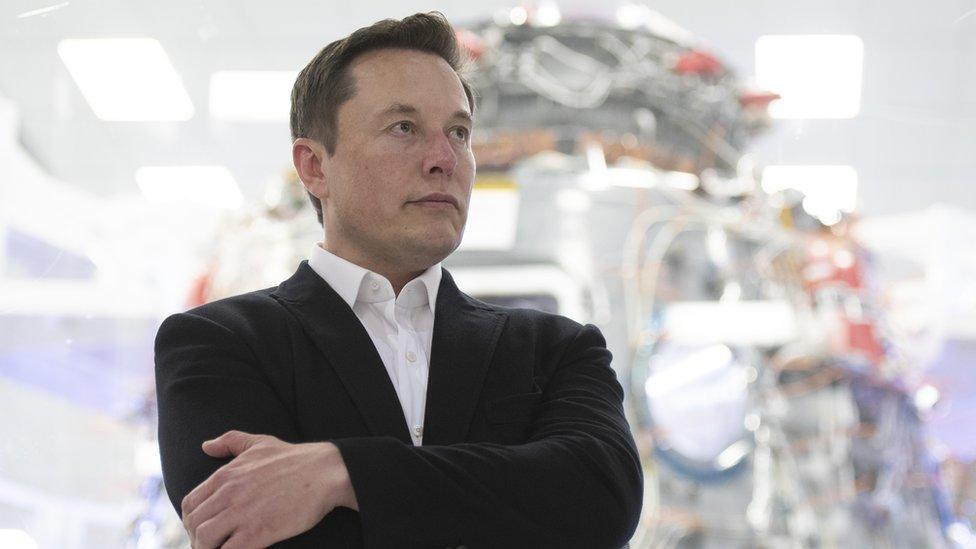 Elon Musk with his arms crossed, wearing a suit