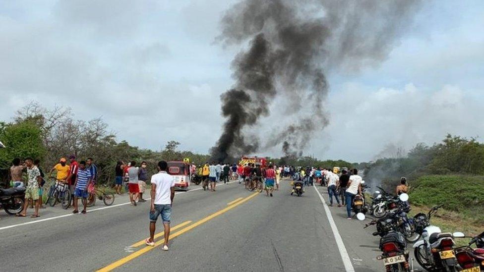 People watch as smoke billows from an overturned tanker truck that caught fire near Pueblo Viejo, Colombia, 6 July