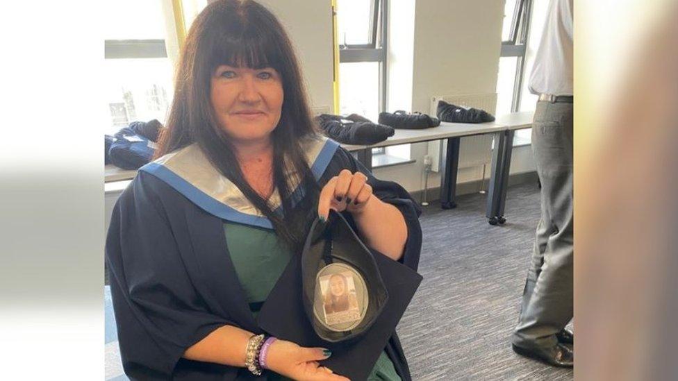 A women with dark hair holding up a graduation cap with a photo of a young girl inside