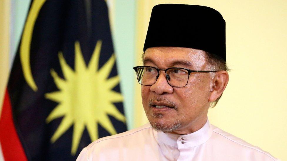 Anwar Ibrahim stands in front of a Malaysia flag