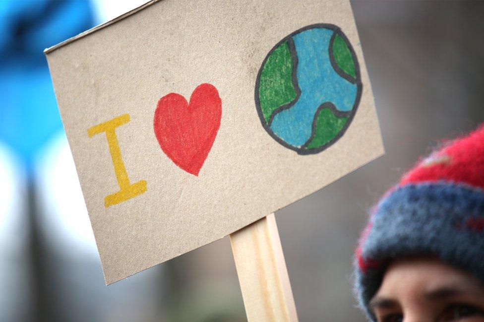 A person holding an illustrated sign that reads: I love the world