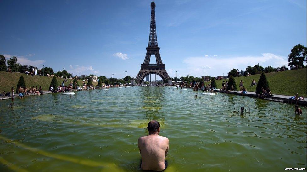 A man sits in a fountain in front of the Eiffel Tower 22 July 2013.