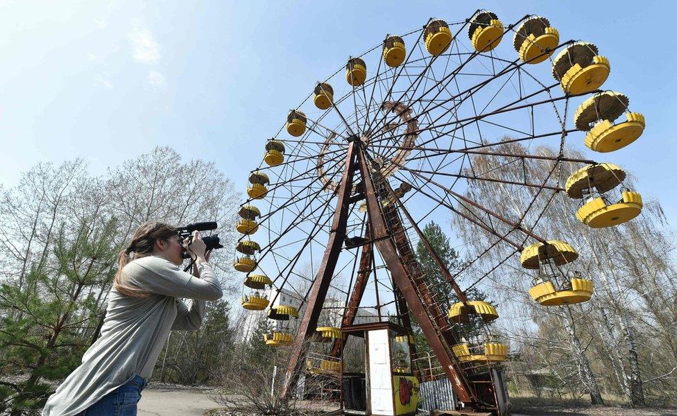 A woman films a Ferris wheel in the ghost city of Pripyat near Chernobyl