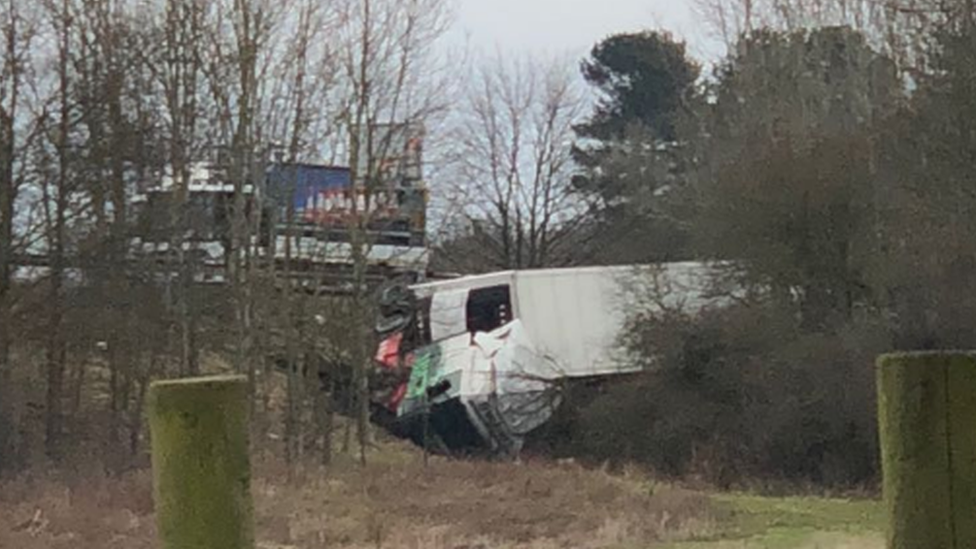 Photograph of a lorry which has left the road before coming to rest on its side