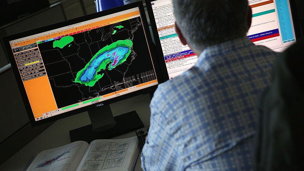 A US National Weather Service employee at work in front of computer screens showing weather data